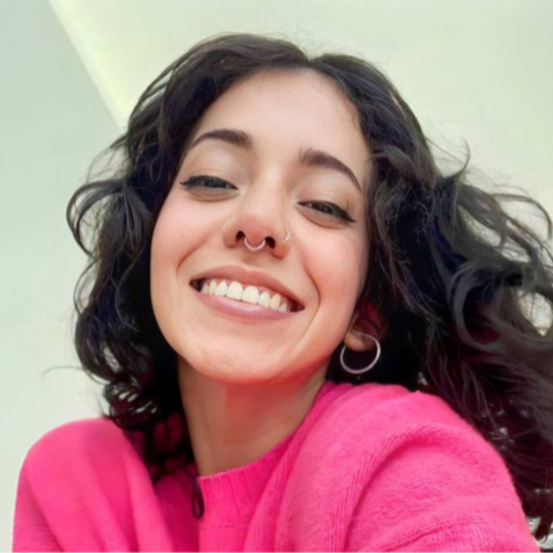 Venessarey, creadora de OnlyFans, conocida por su contenido nude, sonriendo alegremente con un suéter rosa vibrante.